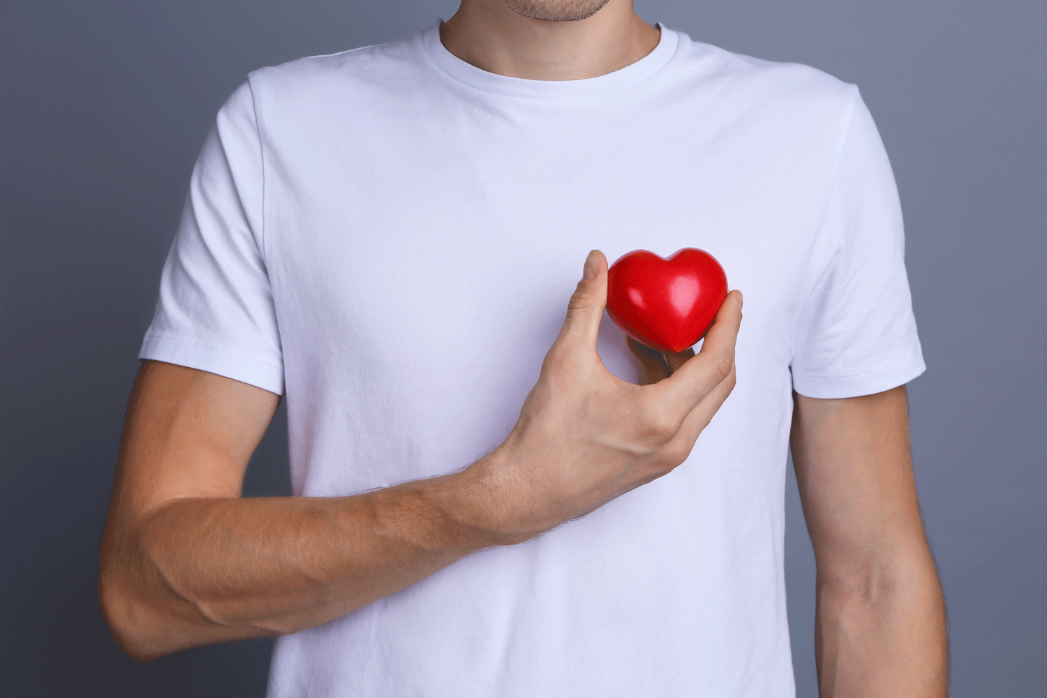 Mann in weißen T-Shirt hält mit seiner Hand ein rotes Herz an die linke Brust