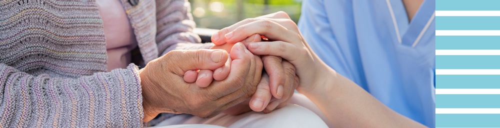 Pflegekraft hält Hände einer Herzpatientin mit hellblauem Balken